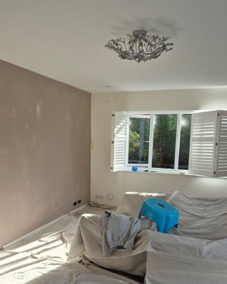 Living room before decorating, with the furniture under dust sheets and walls being prepared